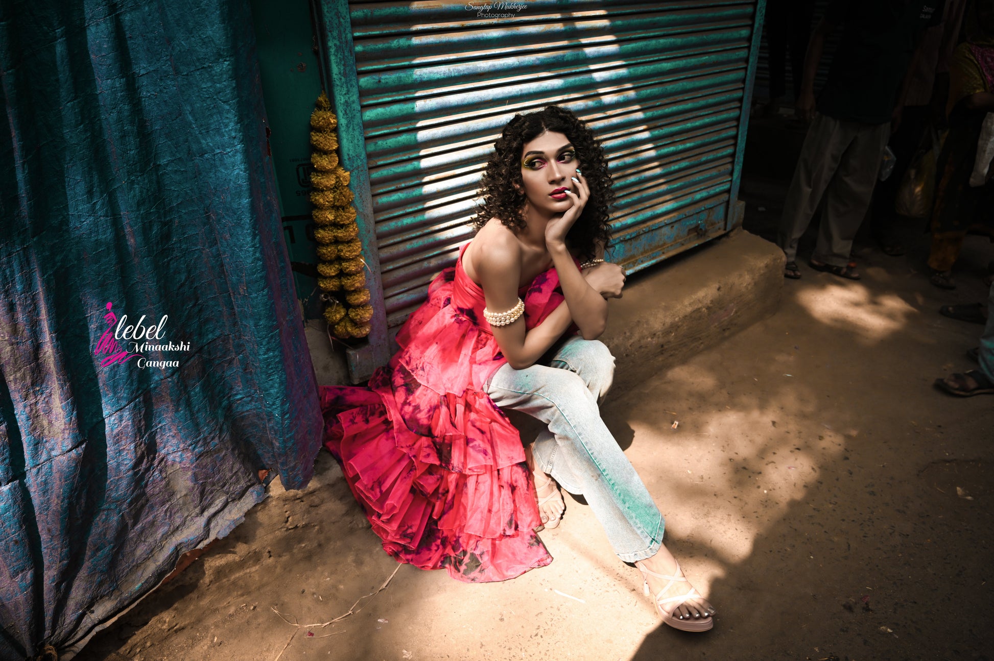 Model in an off-shoulder pink organza ruffle top sitting against a colorful backdrop, showcasing an elegant street style look.